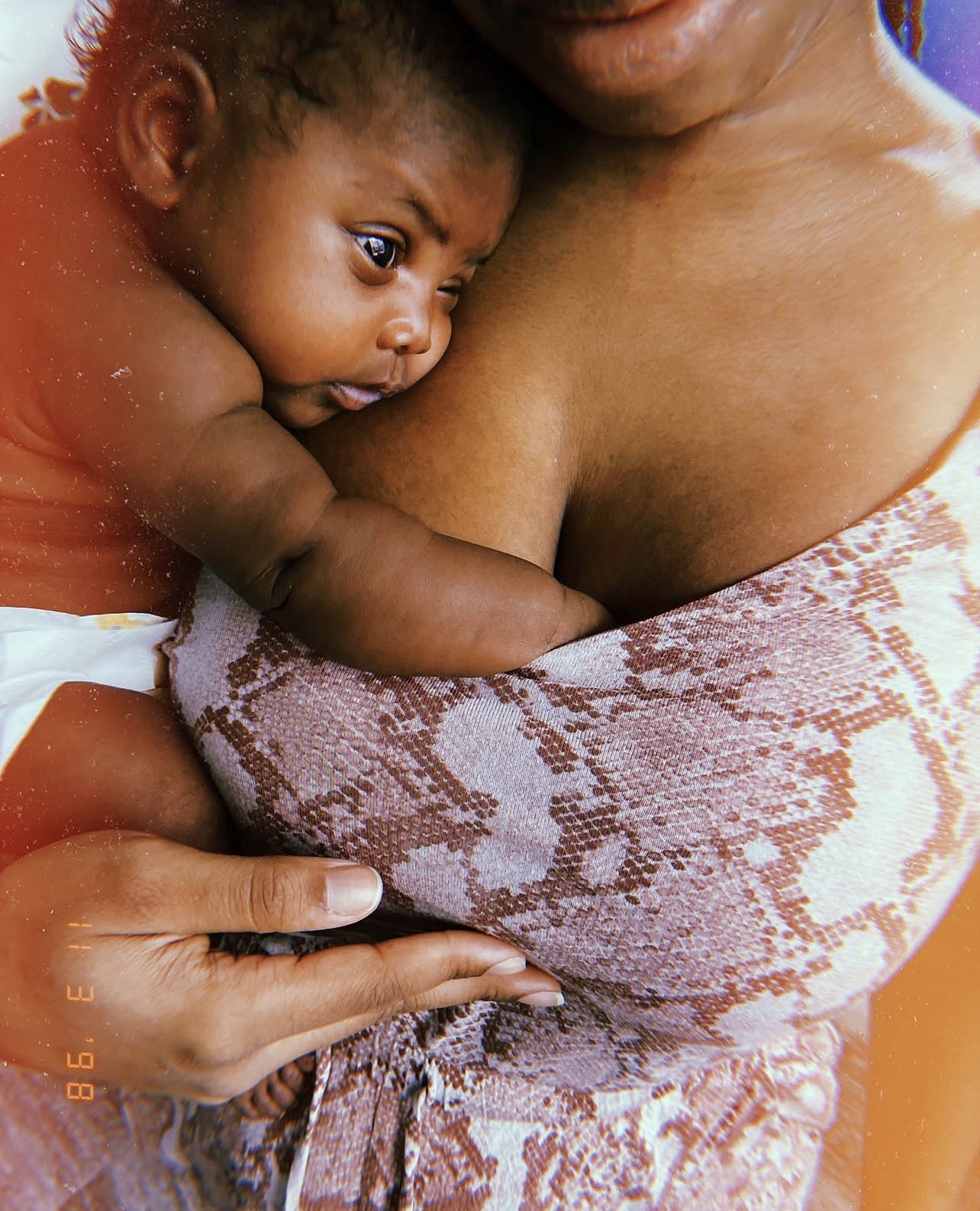 Newborn resting against their mother's chest while feeding, wrapped close in patterned cloth