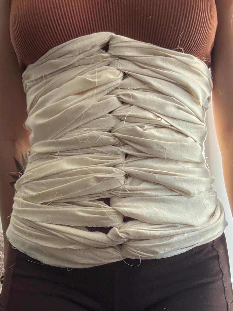 Cream cotton belly-binding cloth wrapped and tied across a mother's abdomen after birth